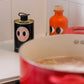 Two bottles with face designs on a kitchen counter next to a pot.