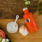 Orange bottle with a face design on a wooden table with vegetables and a bowl.