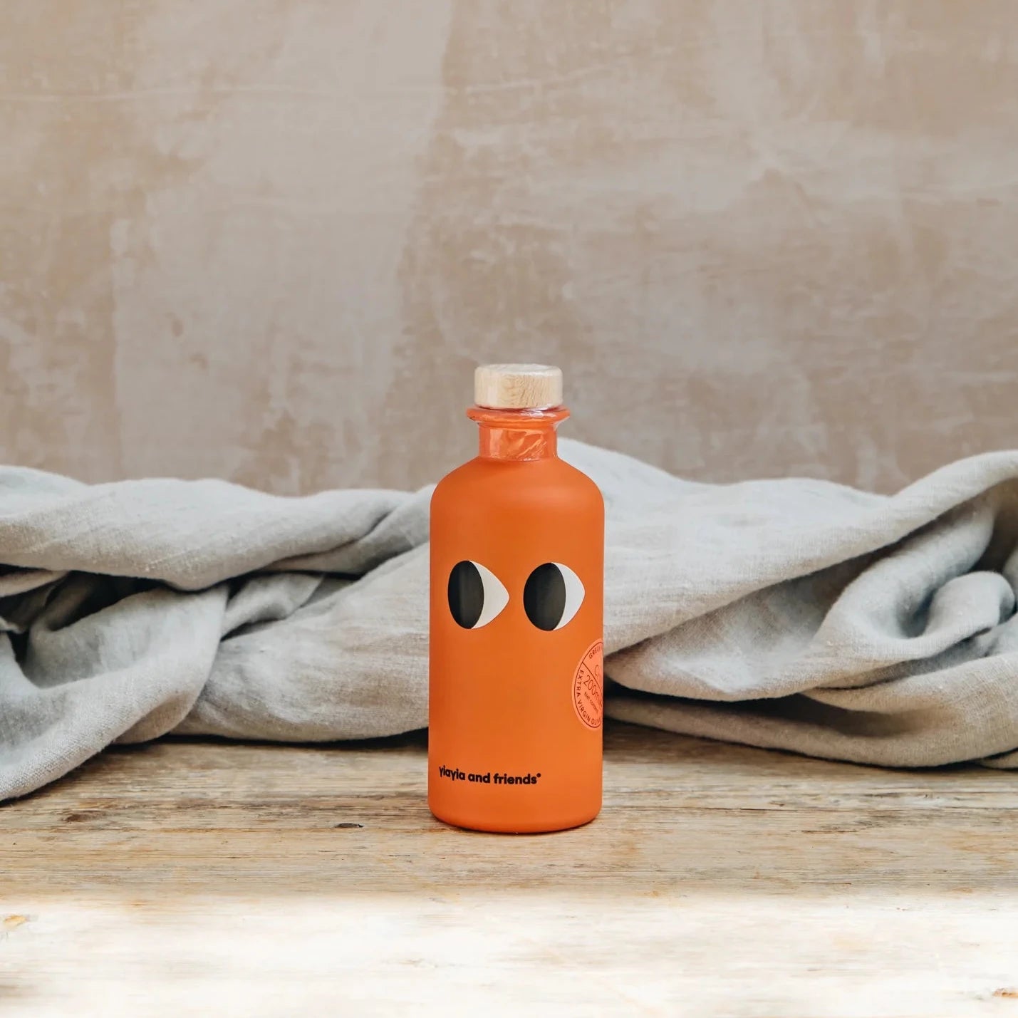 Orange bottle with black eye design on a wooden surface with a beige background