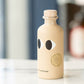 Beige bottle with black eye designs and cork cap on a blurred background