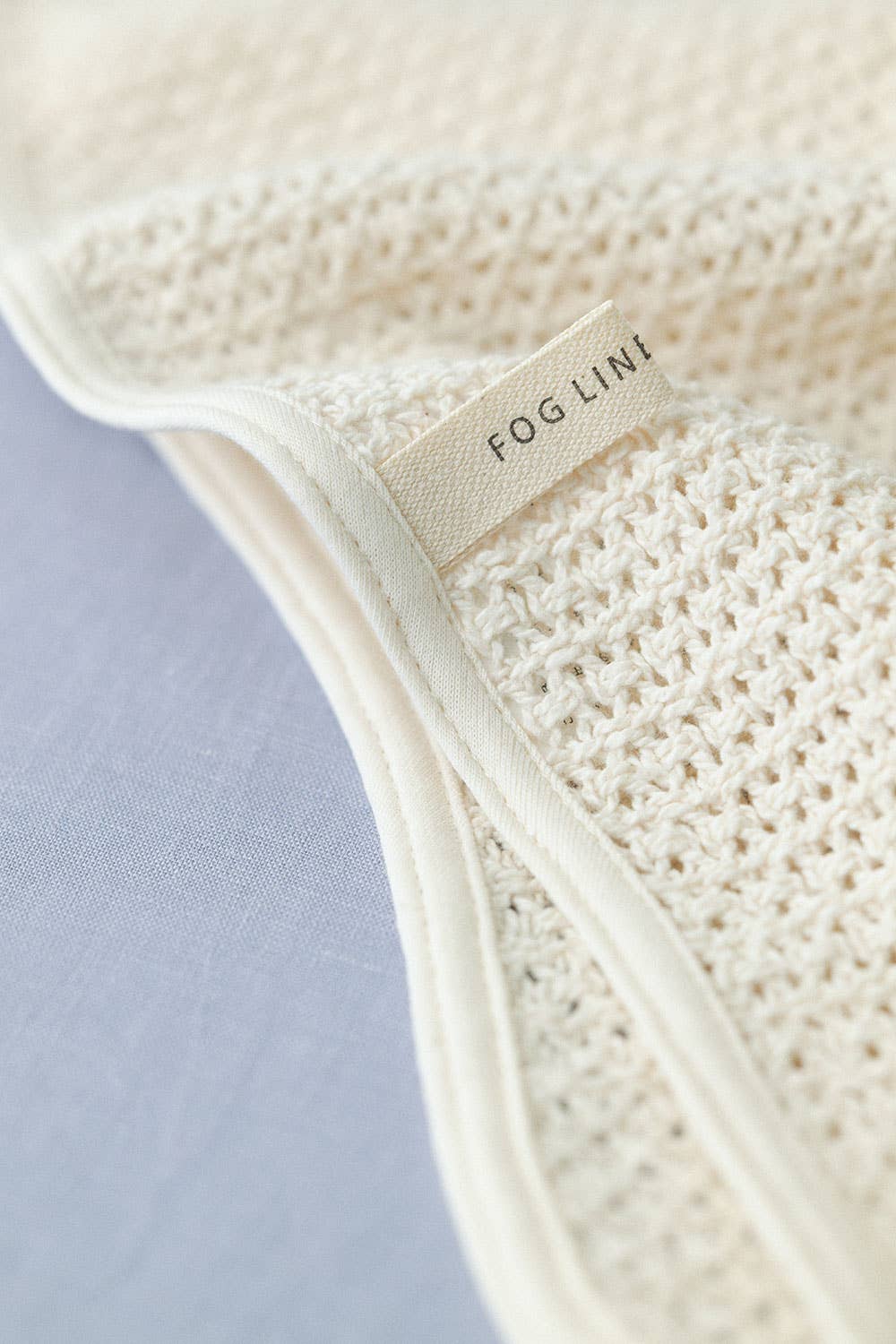 a close up detail image of the fog linen label on the waffle knitted cream blanket, which is sewn into the boarder of the blanket