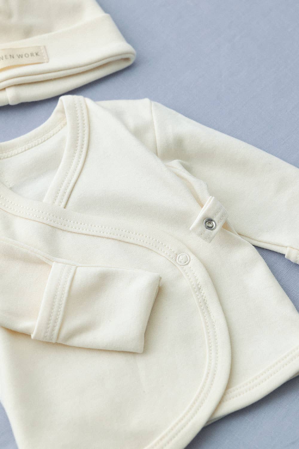 detailed close up of the cotton cream cap and wrap front cardigan showing the small popper detail on the front of the cardigan and fold over hand details on the arms.