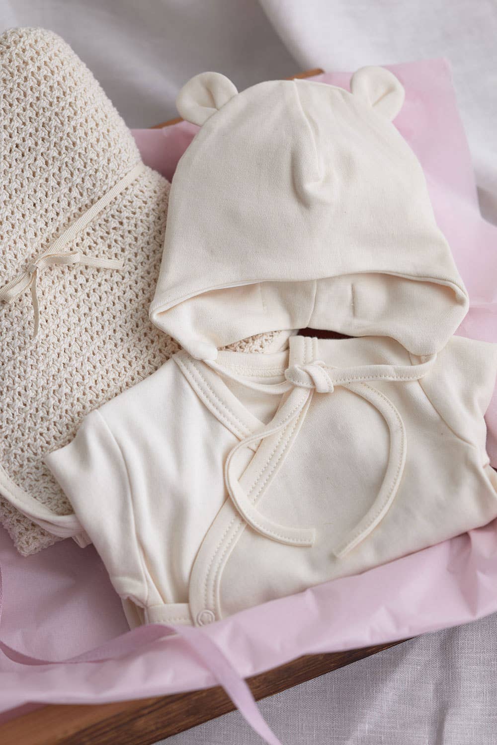 Fog Linen baby pilot hat in natural ivory, made from 100% organic cotton. The hat features a lined interior for comfort, designed for newborns up to 3 months old, sits next to the matching onesie and baby blanket from the same collection.