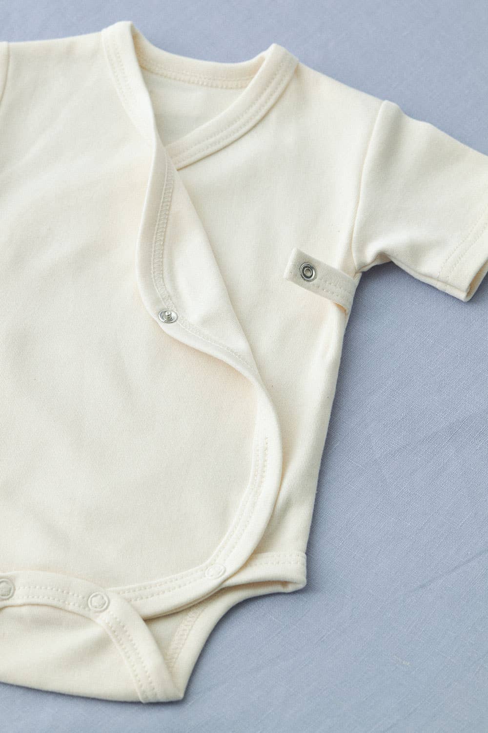 cream white baby romper with short sleeves showing the detail of the popper opening on the side of the wrap front 