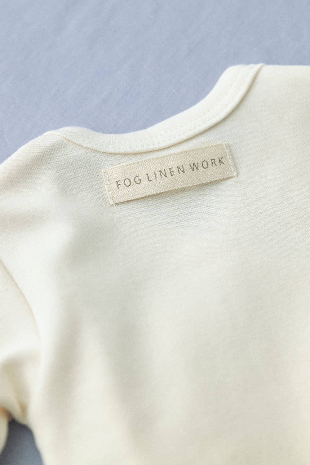 details of the label sewn into the top back of the cream cotton romper, the label spells fog linen work on it n a delicate font