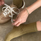 Person tying shoelaces of a brown sneaker wearing green socks on a concrete floor.