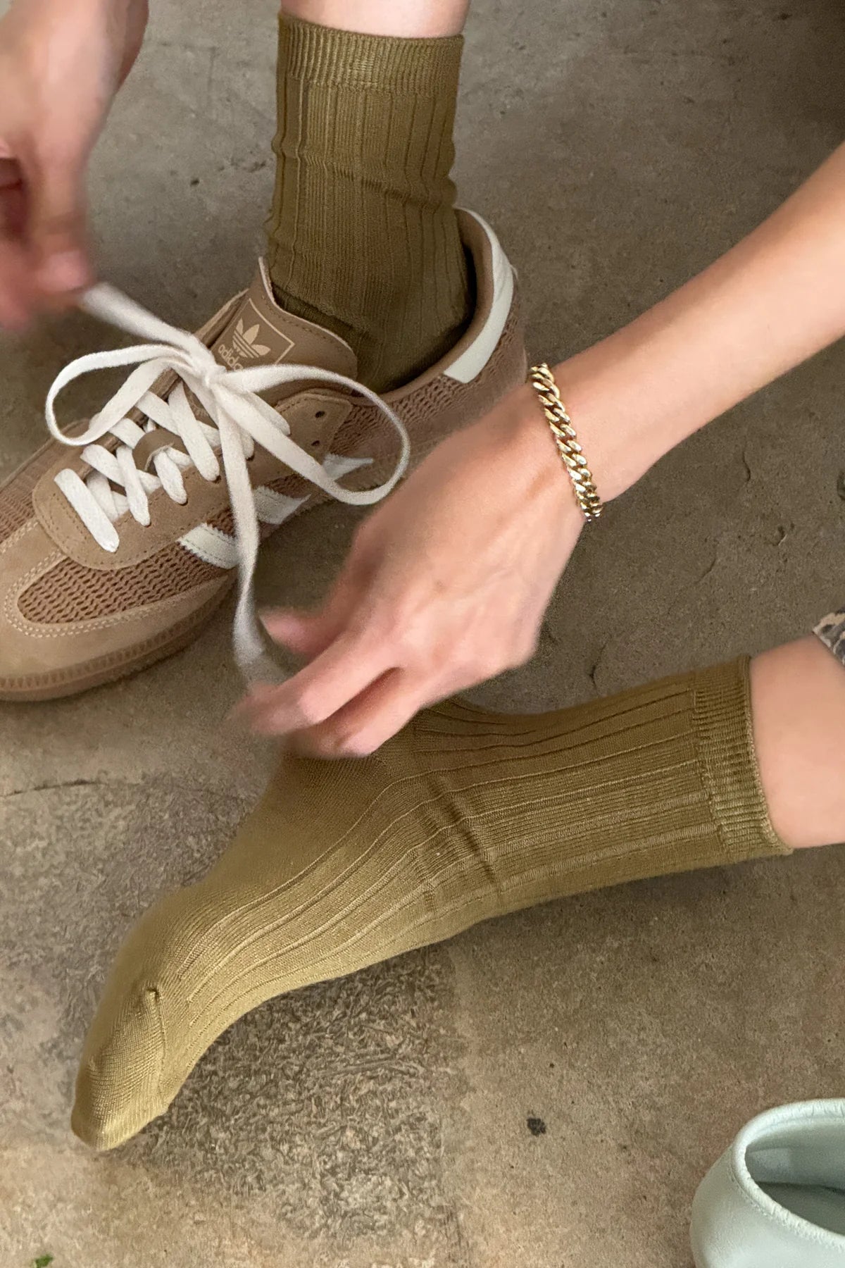 Person tying shoelaces of a brown sneaker wearing green socks on a concrete floor.