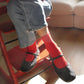 Person wearing red socks and black shoes sitting on a red chair indoors.