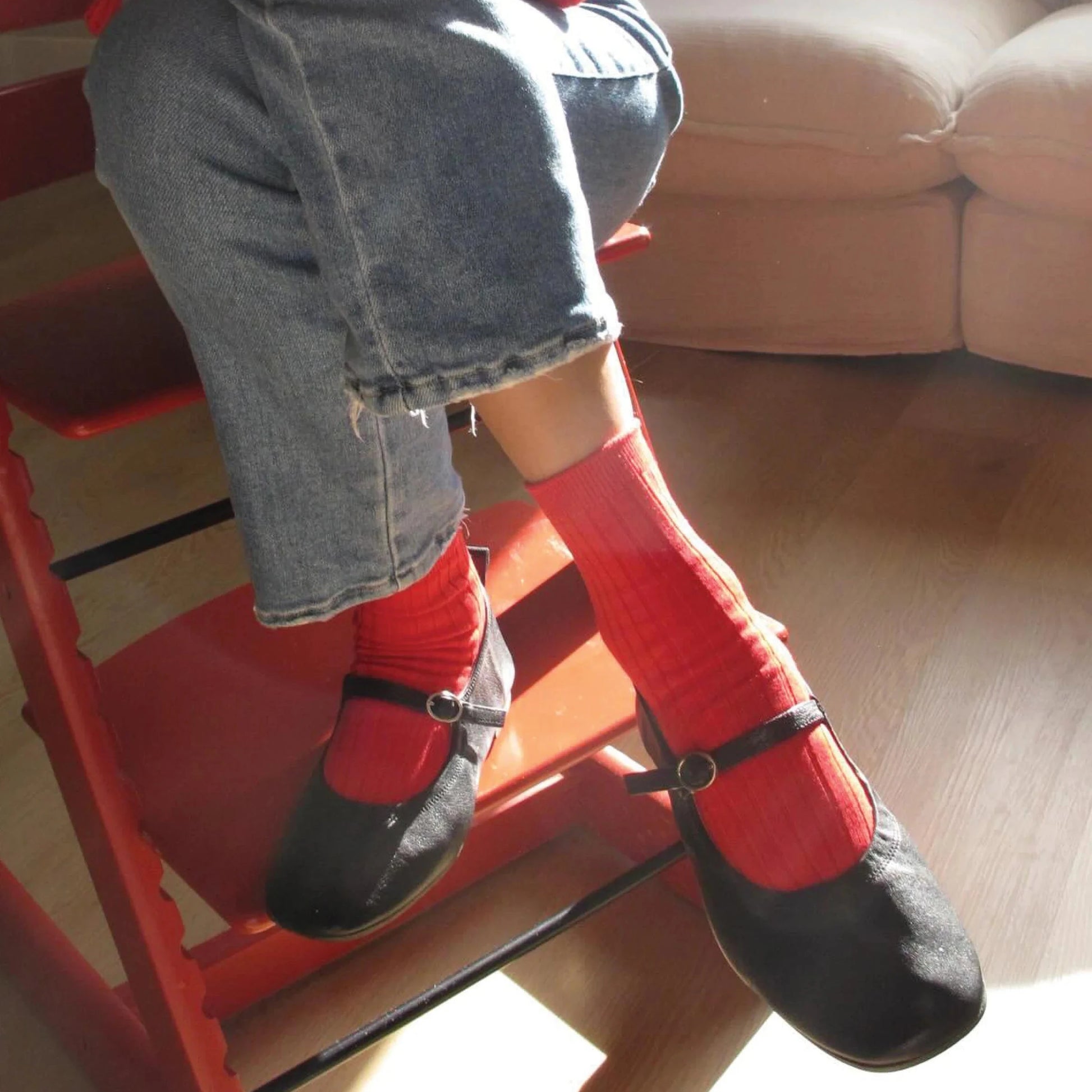 Person wearing red socks and black shoes sitting on a red chair indoors.