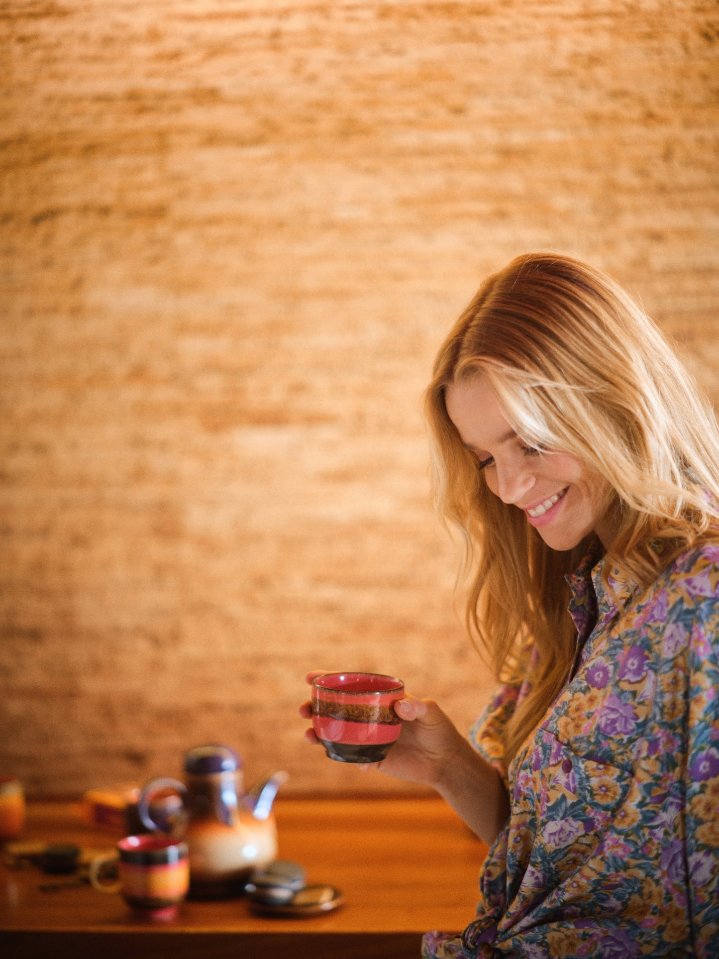 A coffee cup without a handle, with rounded bottom in a pink and speckled orange stripe, with a black bottom