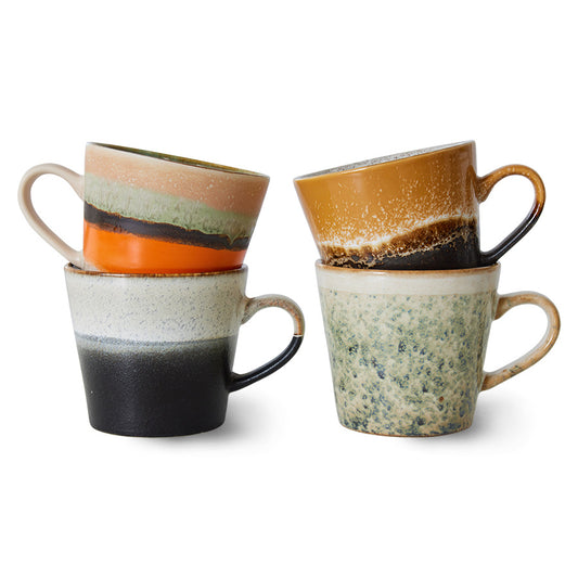 Set of four hkliving verve cappuccino mugs stacked 2by 2. The first is half grey then has a short fade to a speckled white. On top of this one is a mug with half orange and stripes of black and green then cream at the top. Next to these two is a green spackled mug which fades fully to cream at the top. The last one is a dark brown mug with a speckled brown stripe in the middle which fades into a ochre yellow