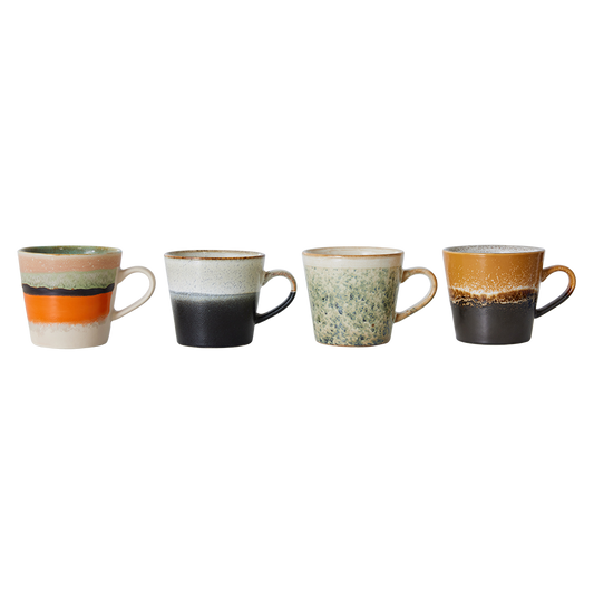 Set of four hkliving verve cappuccino mugs. The first is half grey then has a short fade to a speckled white. Next one is a mug with half orange and stripes of black and green then cream at the top. Then there is a green spackled mug which fades fully to cream at the top. The last one is a dark brown mug with a speckled brown stripe in the middle which fades into a ochre yellow