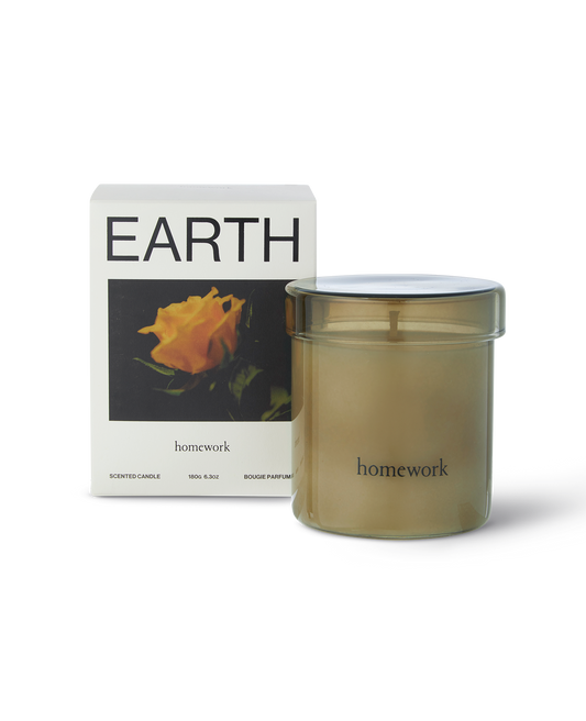 Homework candle in scent Earth. A translucent green glass with lid around the candle the size of a mug with minimal branding reading homework in lower case. Next to the packaging a white box reading Earth at the top and a landscape photograph of an orange rose and the brands name homework under the image