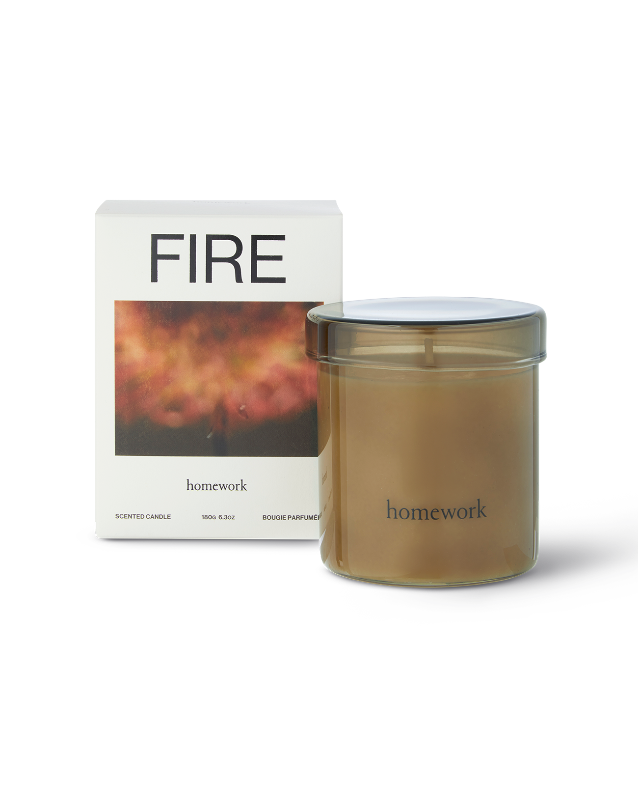 Homework Fire candle in a moss green translucent glass with matching glass lid, with branding of homework along the bottom in lower case text. Next to the packing box, all white with fire spelt across the top, under is a photograph of a blurred fire in red tones. Then the brands name written small underneath the image 