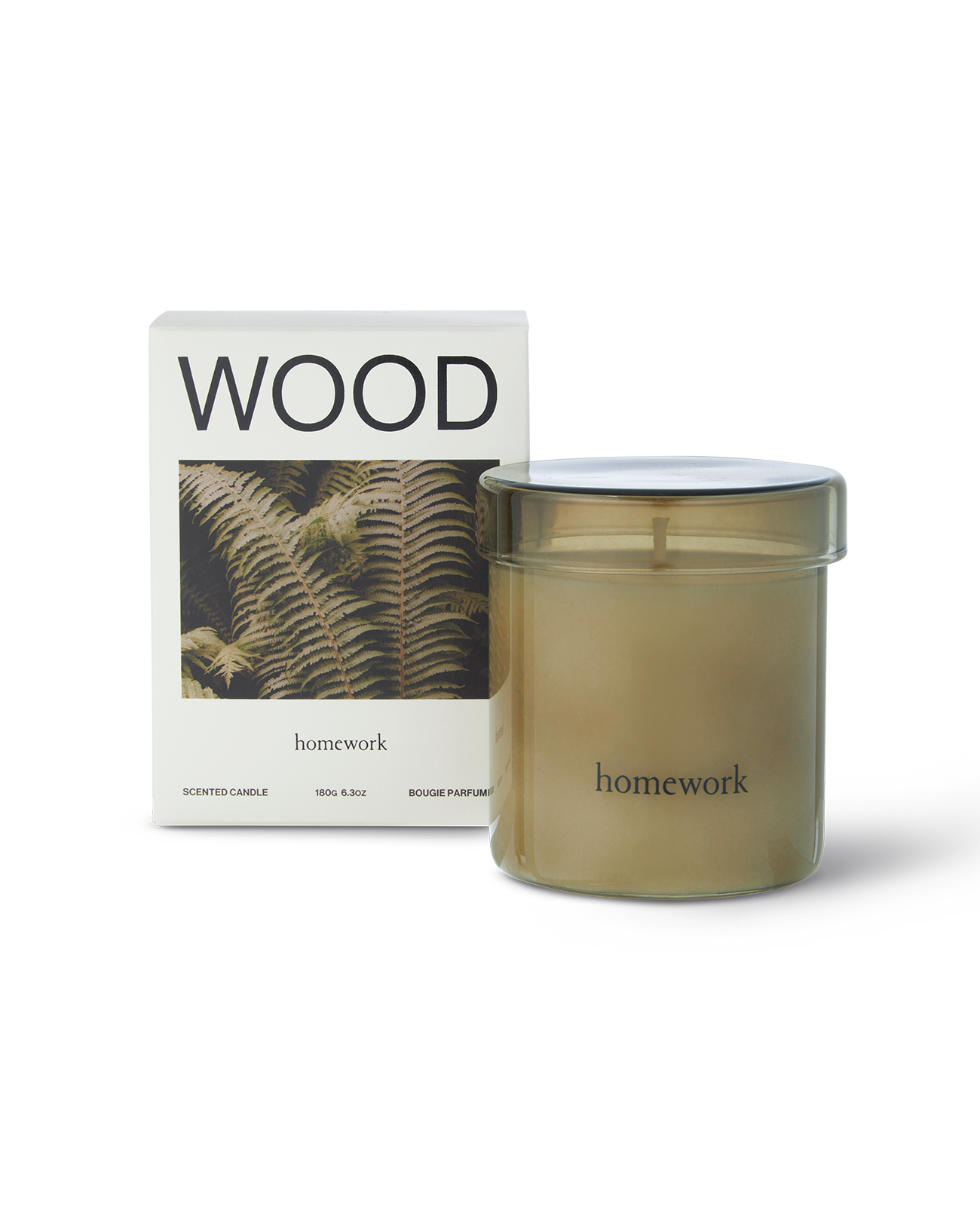 Homework wood scented candle in a moss green cylindrical glass with matching lid. Next to the packaging a white box with wood spelt across the top, under is a landscape image of a brownish green Fern plant. Under this has the branding lower case lettering of homework 