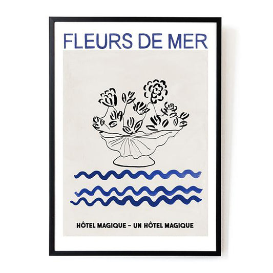 Hotel Magique Fleurs De Mers Print. The background is beige. The flowers and the flower pot is black. The waves below are dark blue in colour. “Fleurs De Mer” is written in dark blue. The print is framed. 