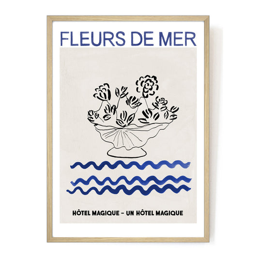 Hotel Magique Fleurs De Mers Print. The background is beige. The flowers and the flower pot is black. The waves below are dark blue in colour. “Fleurs De Mer” is written in dark blue. The print is framed. 