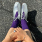 Silver shoes with purple socks on a black asphalt surface