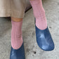 Person wearing pink socks and blue shoes on a concrete floor