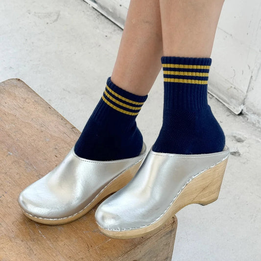 Person wearing navy socks with yellow stripes and silver clogs on a wooden block.