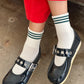 Person wearing navy blue shoes with buckles, white socks with green stripes, and red pants on a concrete floor.