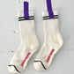 White socks with purple tags and red text on a gray background