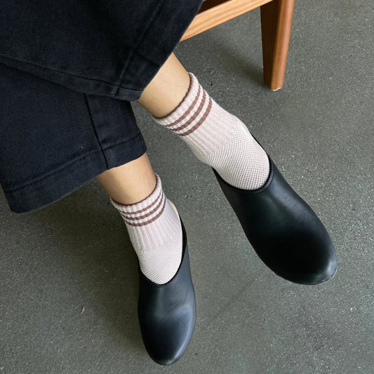 Person wearing black shoes and white socks with red stripes, sitting on a wooden chair.