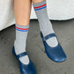 Person wearing gray socks with red and blue stripes and blue shoes on a concrete floor.