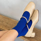 Beige shoes with blue socks worn by a person sitting on a wooden bench.
