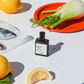 Perfume bottle with lemons, fish, and fennel on a white surface