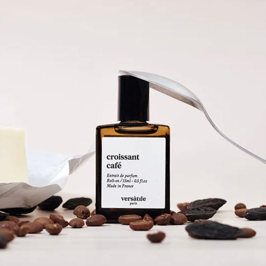 Perfume bottle labeled 'croissant cafe' by Versatile Paris with coffee beans on a light background