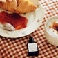 Bottle of croissant cafe perfume on a checkered tablecloth with a croissant and coffee.