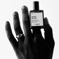 Hand holding a 'Gueule de Bois' Versatile Paris perfume bottle on a white background