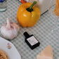 Perfume bottle labeled 'vivienne' on a table with a yellow bell pepper, garlic, and pasta.