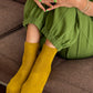 Person wearing green pants and yellow socks sitting on a brown couch.