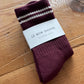 Maroon socks with white stripes on a wooden surface, branded 'Le Bon Shoppe'.