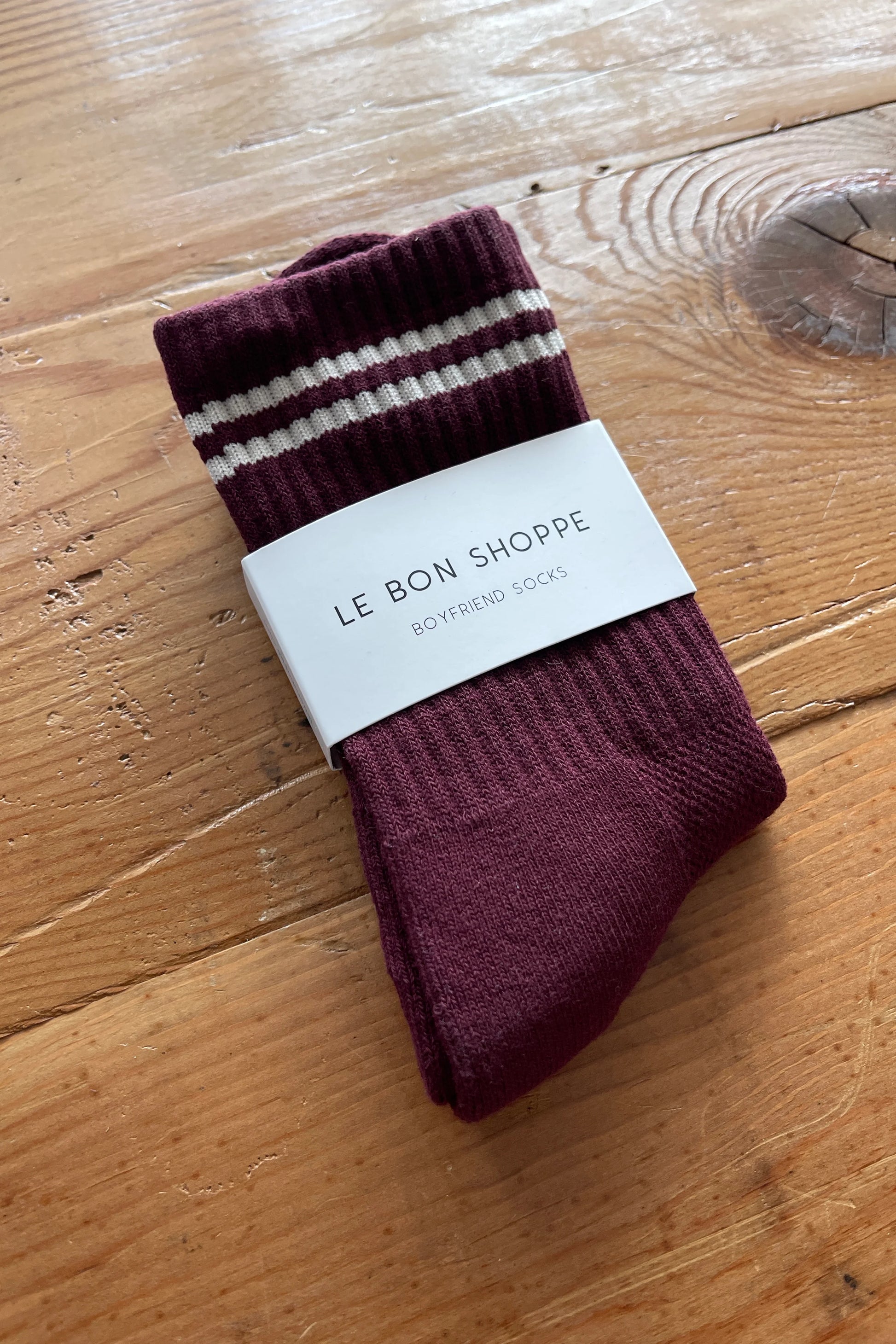 Maroon socks with white stripes on a wooden surface, branded 'Le Bon Shoppe'.