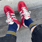 Red sneakers with white laces and blue socks with yellow stripes on a concrete surface.