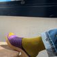 Person wearing a purple sandal and yellow sock, sitting on a chair with a palm tree in the background.