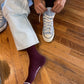 Person tying shoelaces on a light blue sneaker on a wooden floor.