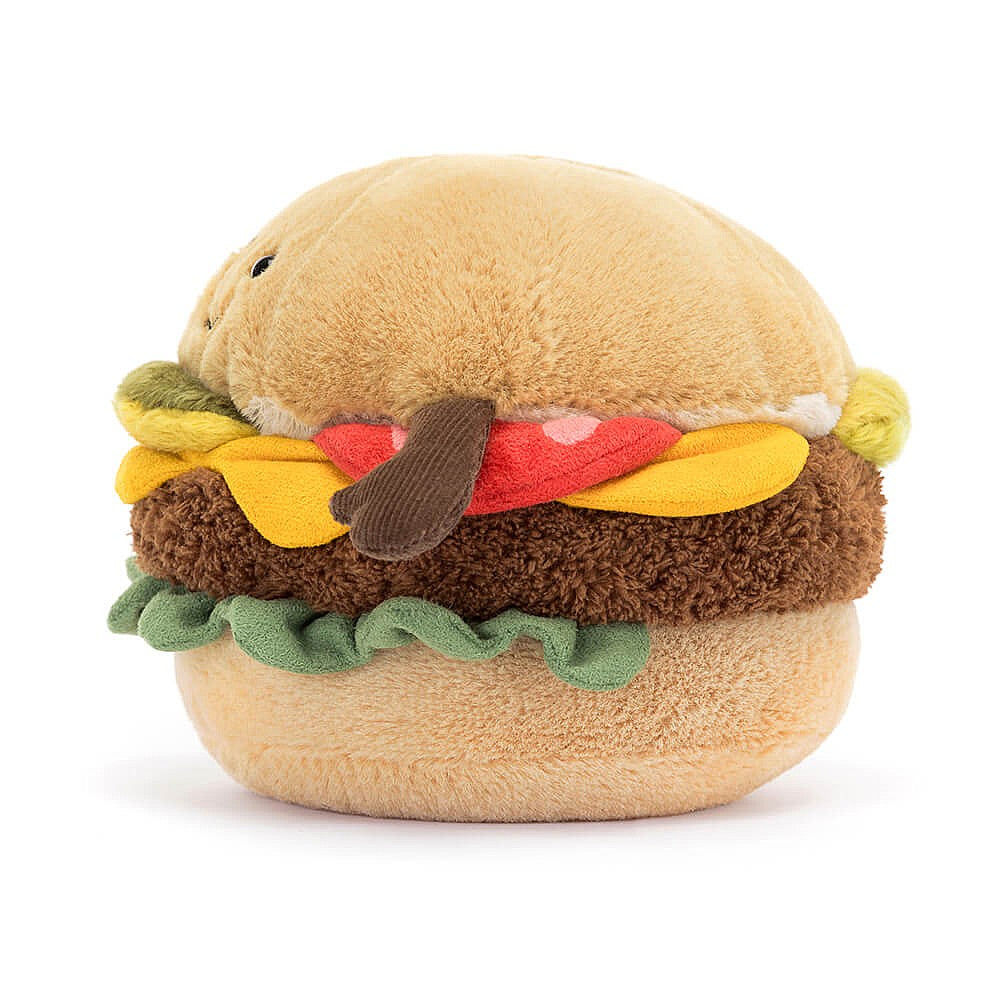 The side of a plush toy in the shape of a cheeseburger showing the beige bun with a brown small arm coming out the side of it. The layers of the burger which are red tomato, yellow cheese, a brown patty, green lettuce and then the bottom beige bun. This is against a white background. 