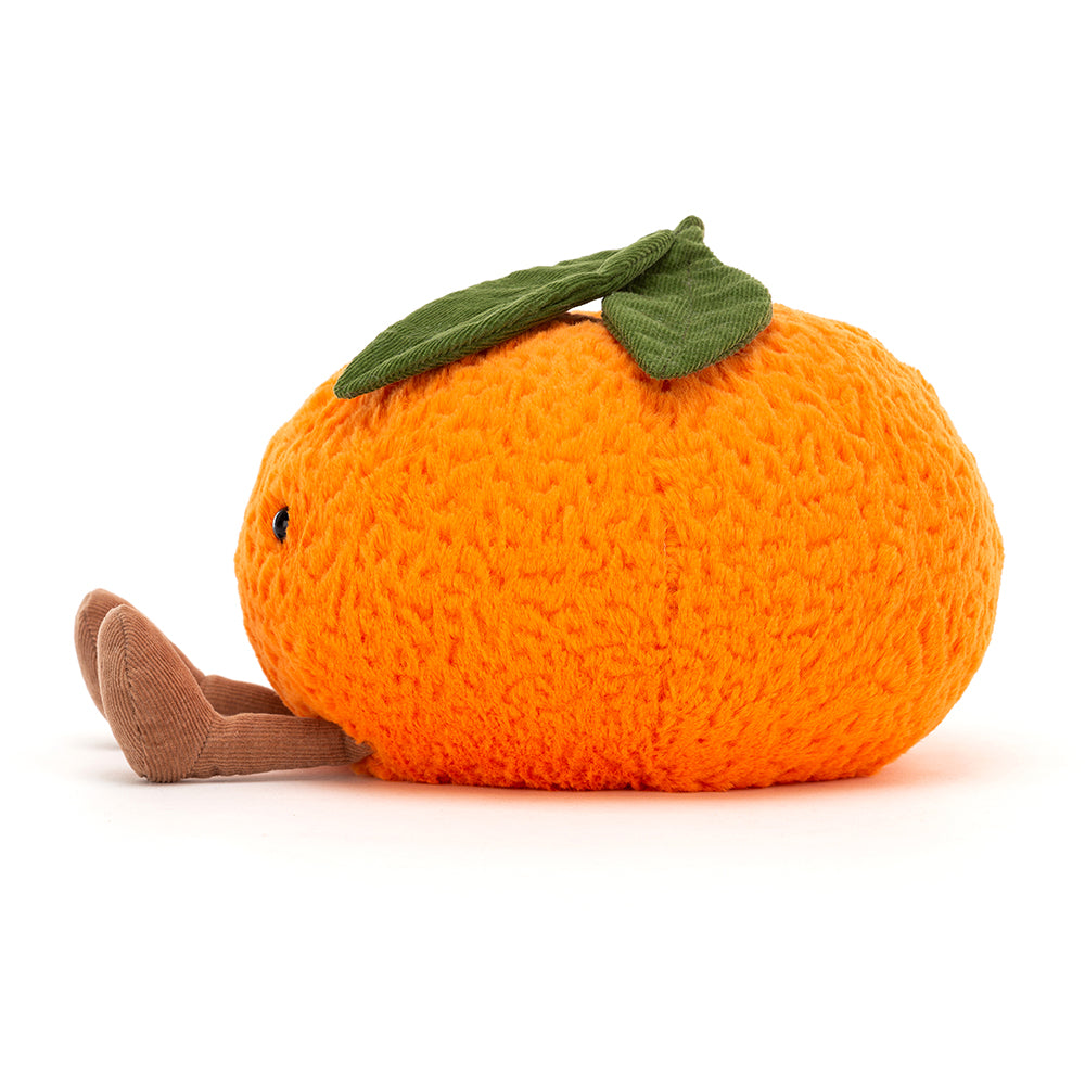 The side of plush toy in the shape of an orange. The orange, which is also the colour orange is textured and has a green stem with two green leaves coming out the top of it. The orange has a black small and two eyes, which appear to be  beads. At the bottom of the orange there are two brown feet, making the orange 'sit down'. This is against a white background. 