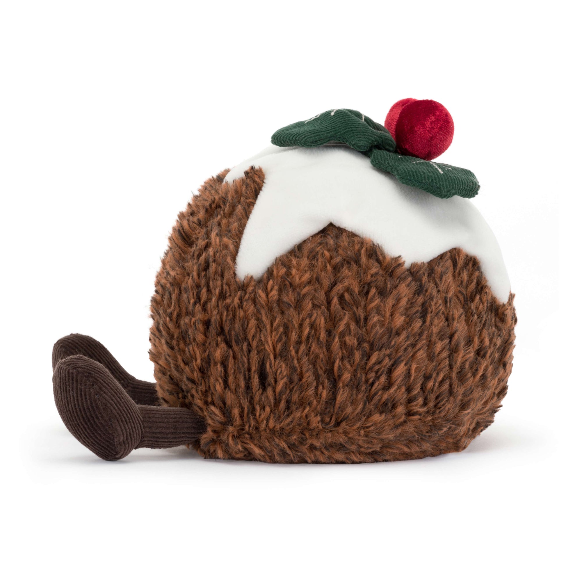 A plush Jellycat Amuseables Christmas Pudding with a textured brown body, white icing drizzle, two red berries, and a green leaf, sitting on a white surface. Shown from the side