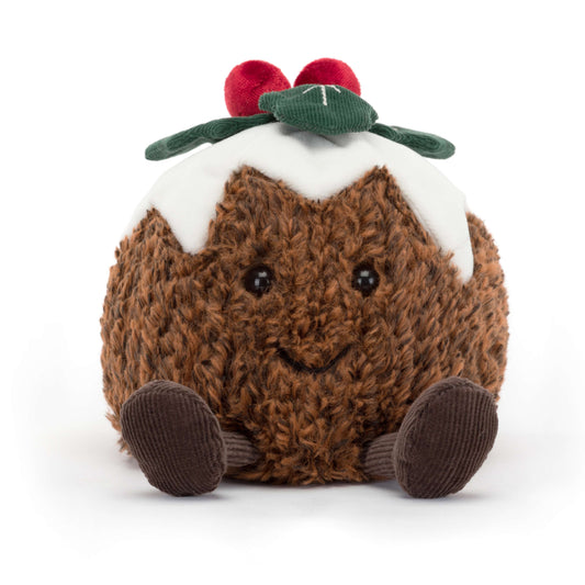 A plush Jellycat Amuseables Christmas Pudding with a textured brown body, white icing drizzle, two red berries, and a green leaf, sitting on a white surface.