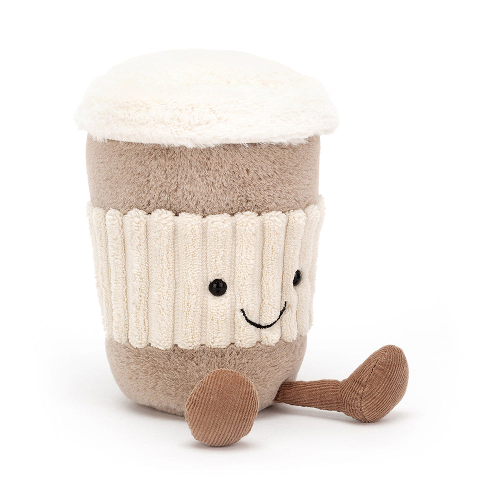 A soft, plush coffee cup with a friendly face and textured lid, featuring a little handle. The coffee cup is part of the Jellycat Amusables collection, designed to resemble a to-go coffee cup, and has a cozy, cuddly appearance. Shown sitting from a side angle