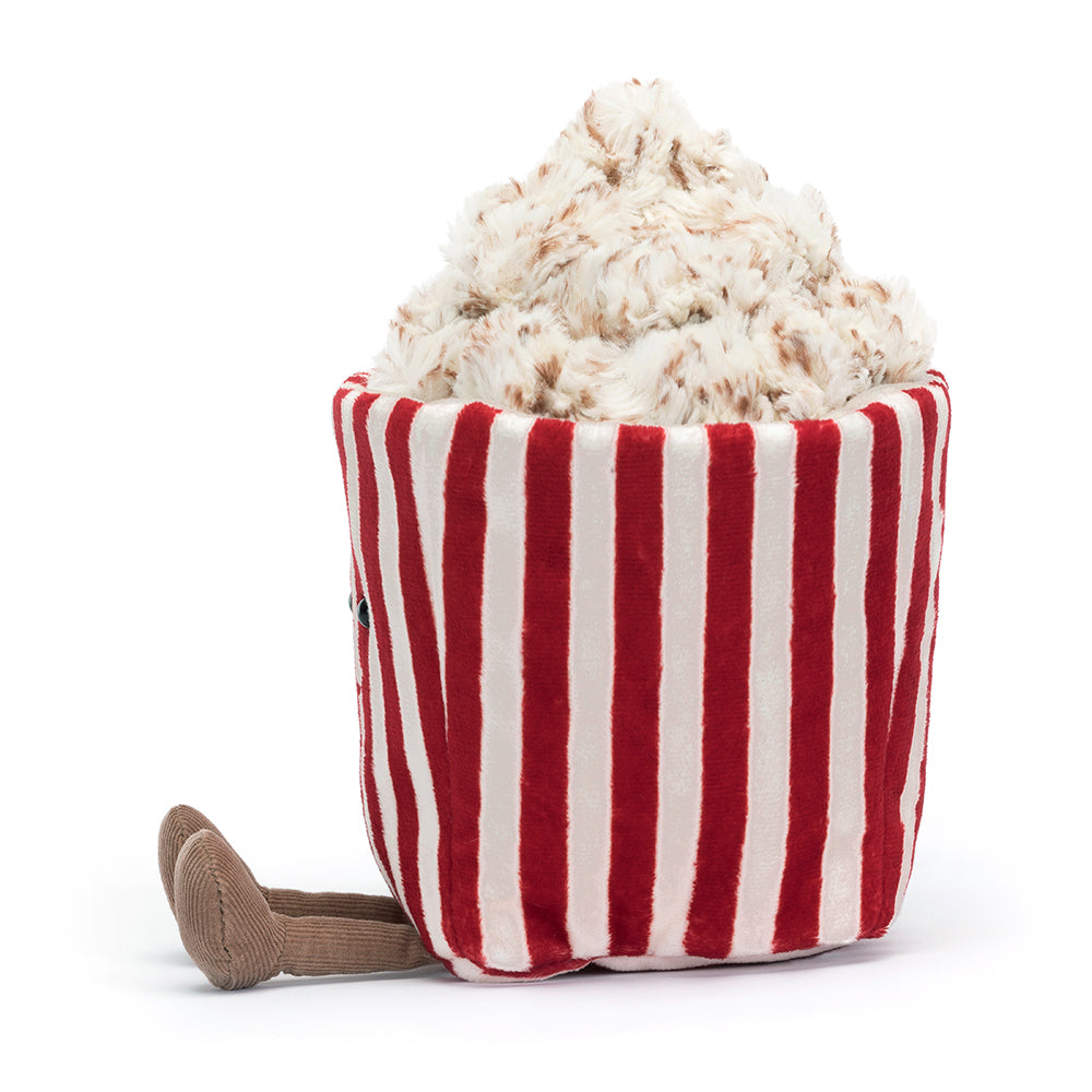 Side view of A whimsical Jellycat Amuseables Popcorn plush toy featuring a red-and-white striped tub with a smiling embroidered face, overflowing with fluffy, buttery popcorn pieces on top, and playful brown corduroy legs. Perfect for movie night vibes.