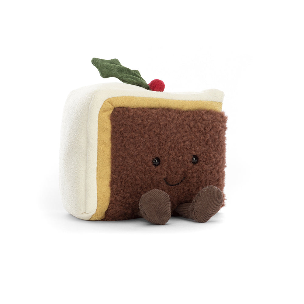 A soft, plush toy shaped like a slice of Christmas cake, featuring a smiling face, colorful icing, and festive decorations. The Jellycat Amuseables Slice of Christmas Cake is designed for cuddling and imaginative play, capturing the joyful essence of holiday treats. Perfect for children and collectors, it adds a delightful touch to any festive collection. Shown from a side angle