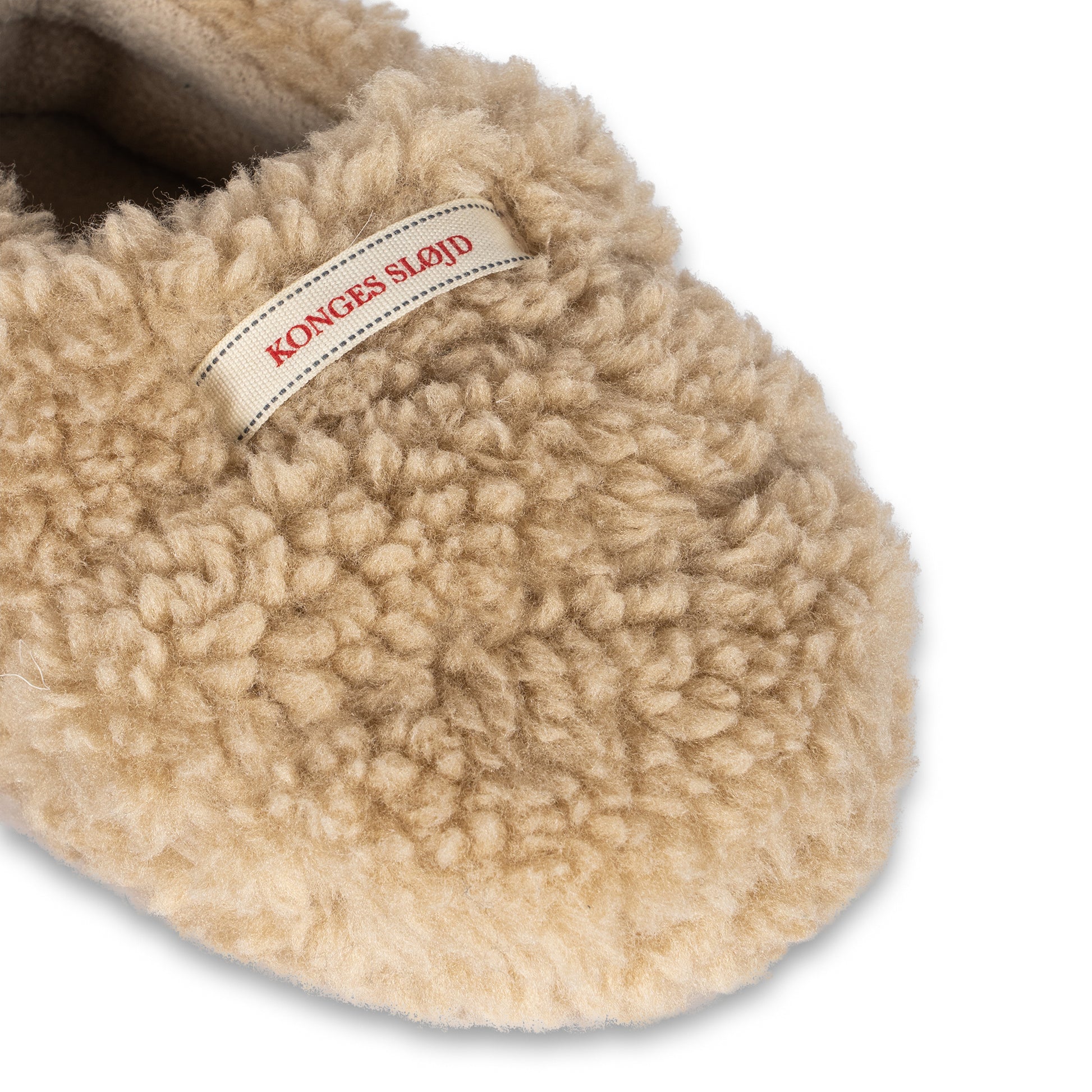 A close-up of the Konges Sløjd Globe Footies, highlighting the fluffy sherpa fabric and the detailed Konges Sløjd label stitched on the upper part.