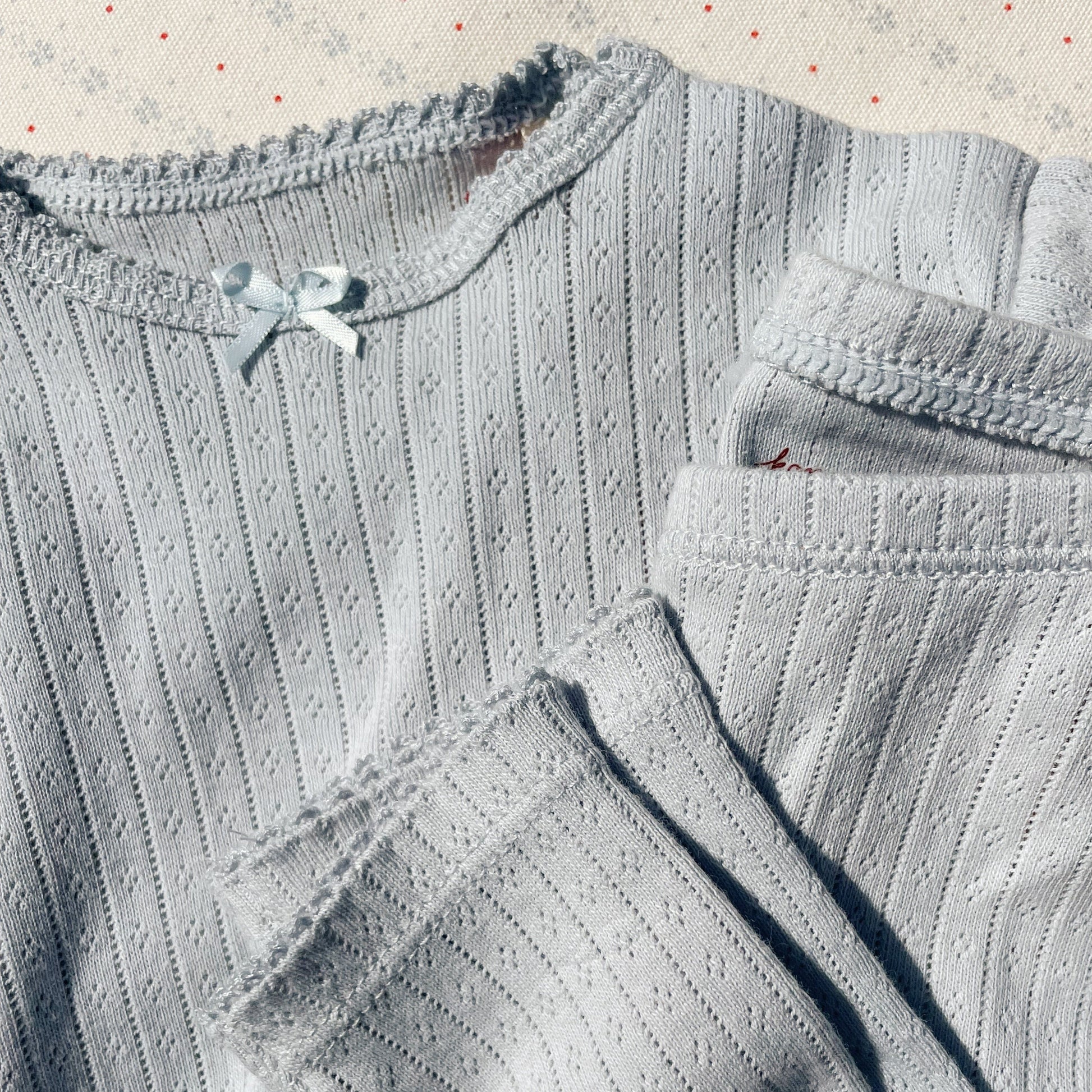 A close-up of the Konges Sløjd Minnie Body in gray dawn, highlighting the fine lace trim, bow detail, and delicate pointelle knit fabric.