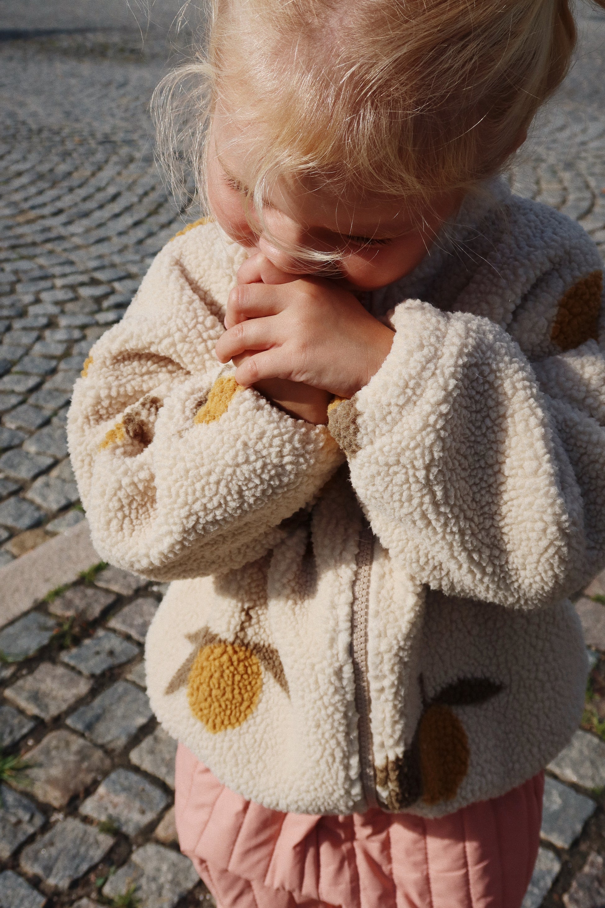 A close-up of a child wearing the soft fleece jacket with a lemon pattern, standing outdoors.